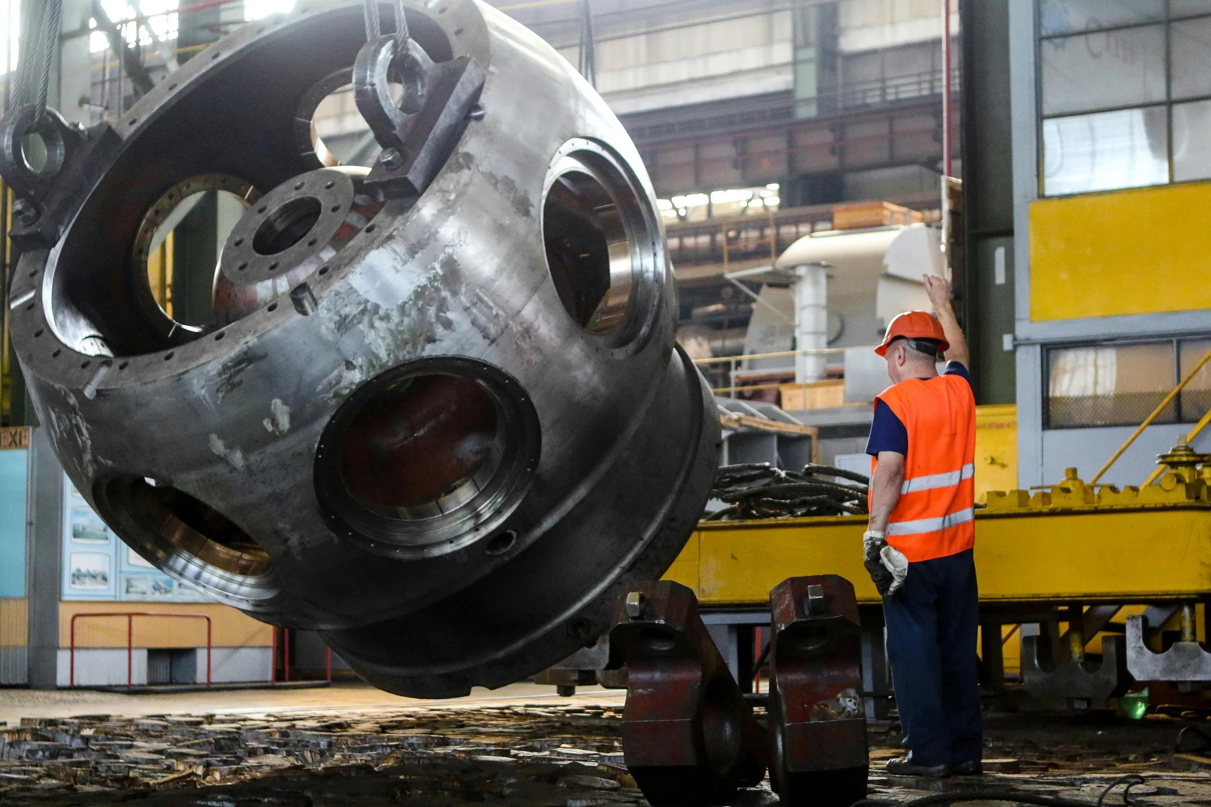 Rigging professional directing the movement of a large industrial metal casting in a factory